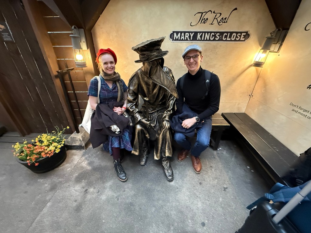 Two people pose with a "plague doctor" sculpture 