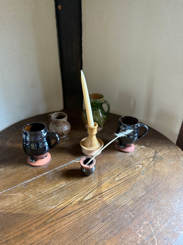 A quill sits in a stand next to a candle and some cups