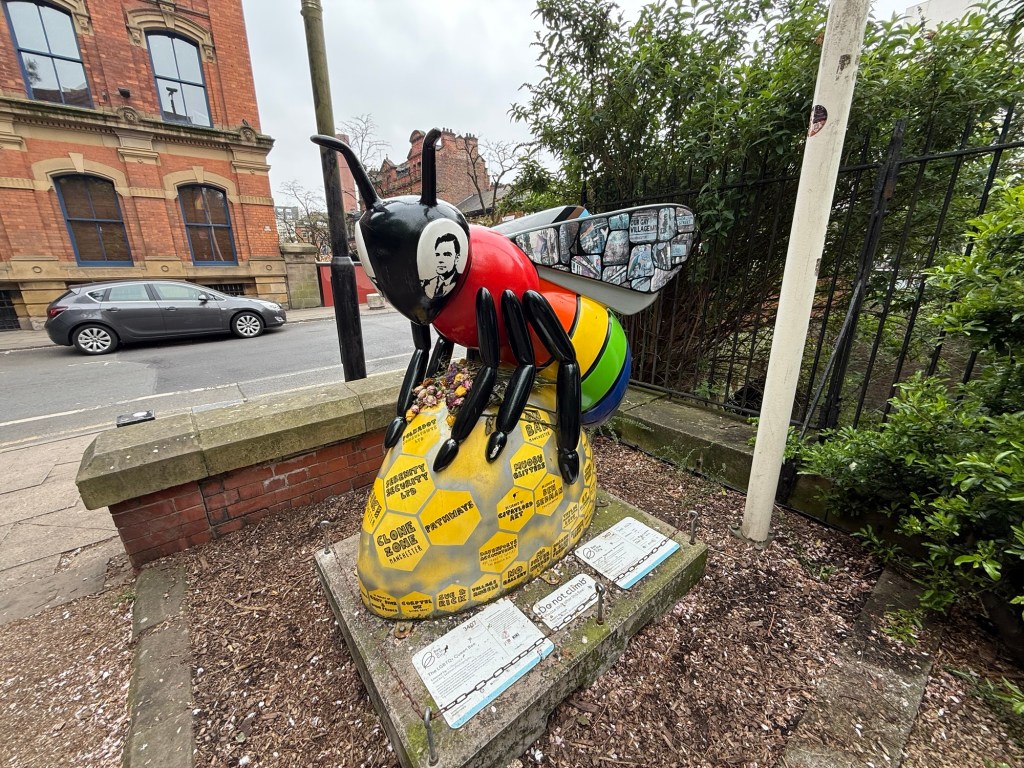 A sculpture of a bumble bee atop a drop of honey, possessing the signatures of notable Queer artists in Manchester
