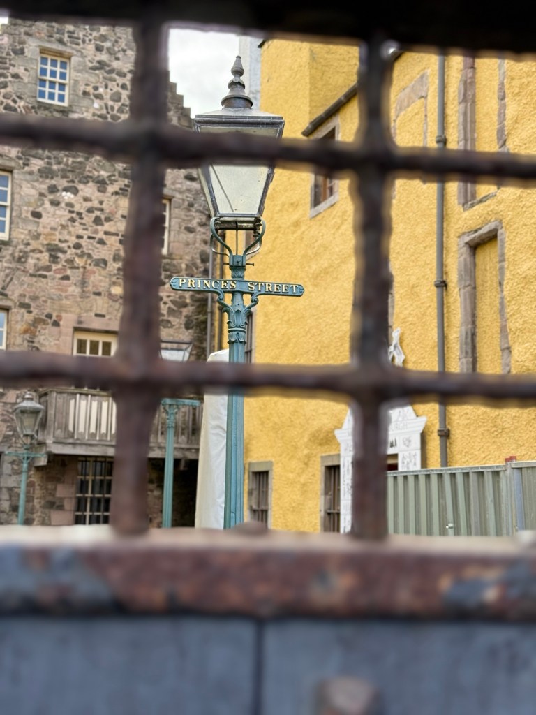 A view through a gated door showing a Street lamp with "princes street"