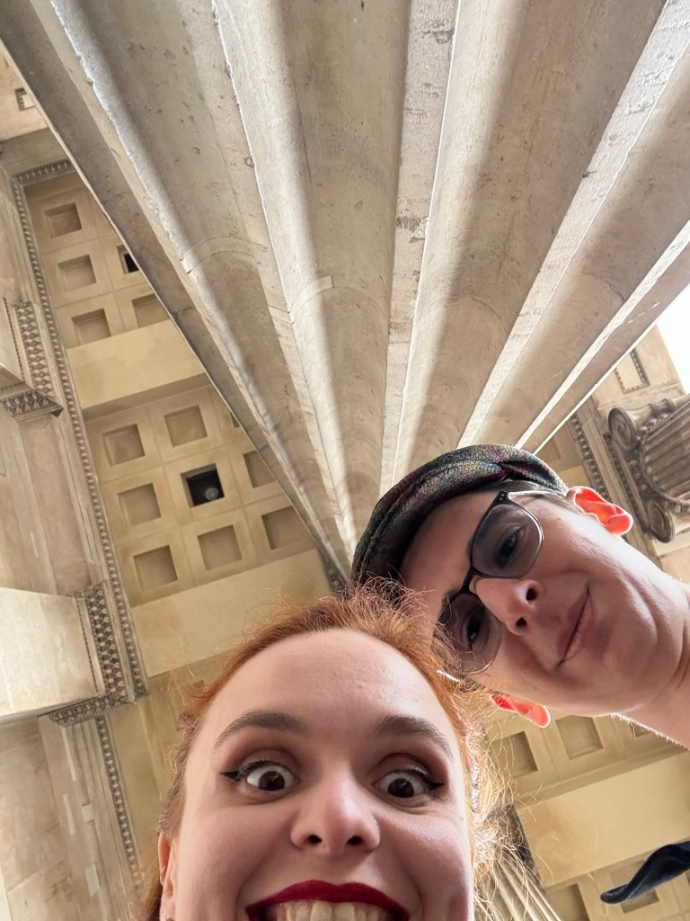 Two people pose with the camera facing to the ceiling of the front of the British museum so that all the dimensions appear comical
