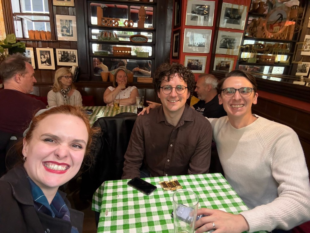Three people pose at a table in a London pub