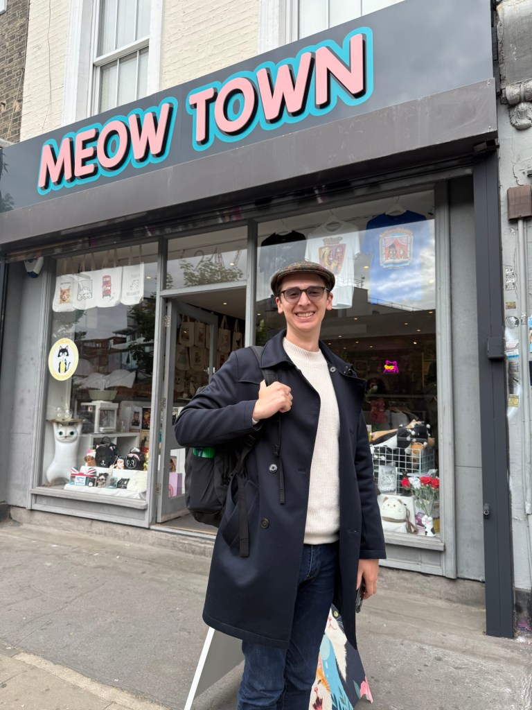 A man poses in front of a store called “Meow Town”