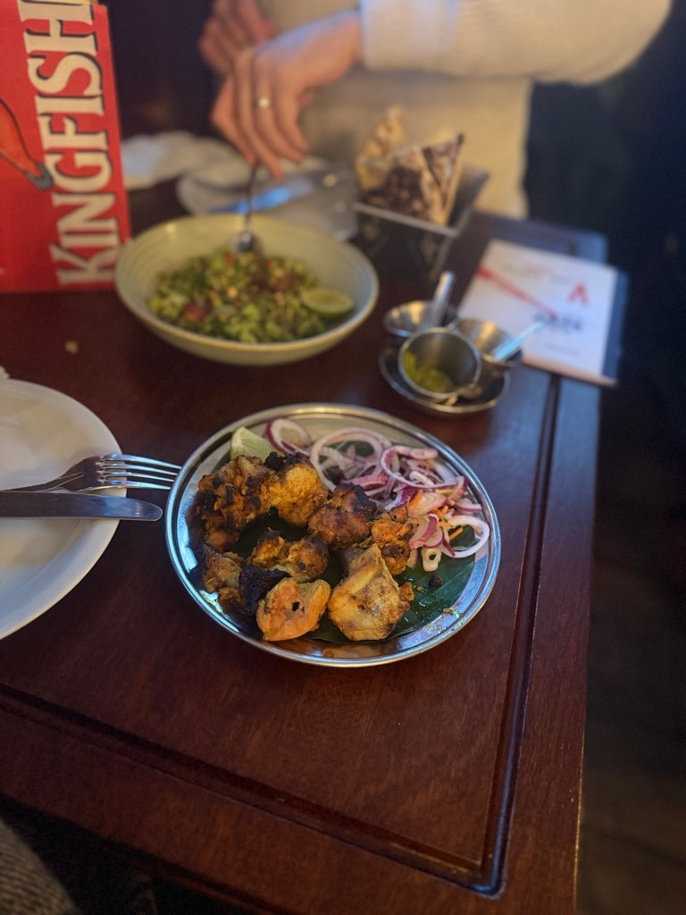Two dishes of spiced food sit atop a well worn restaurant dining table