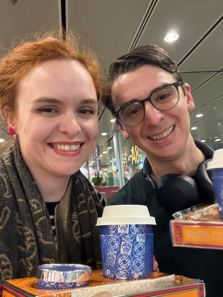Two people pose with coffees in hand